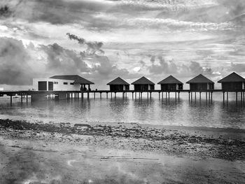 Stilt houses on beach by sea against sky