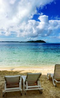 Deck chairs on beach against cloudy sky