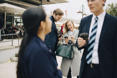 Smiling entrepreneur by male colleague using smart phone in city