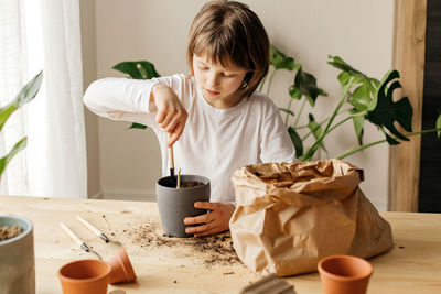 A cute little girl is transplanting a home flower at home. pour soil into the pot. 