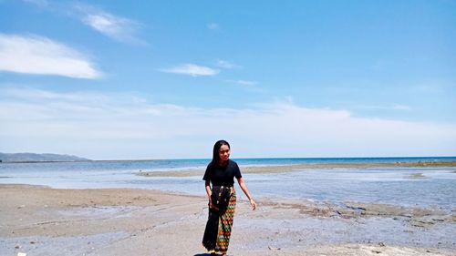 Rear view of woman standing at beach against sky