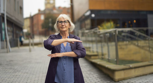 Portrait of senior woman gesturing while standing on footpath