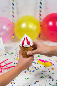 Mom's hand passes an ice cream cone to a child's hand on the background of a birthday party.