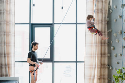 Young boy indoor rock climbing with his father instructor. hobby or home sport concept