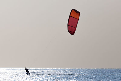 Person paragliding in sea against clear sky