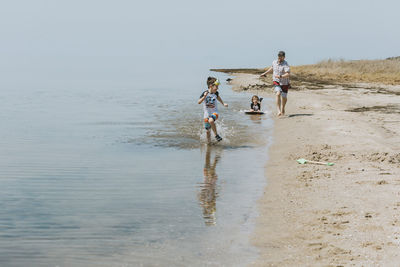 Father pulling boy sitting on surfboard while running behind son in sea during sunny day