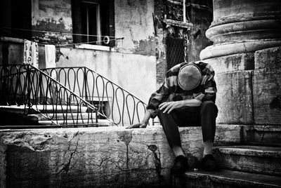 Man sitting on retaining wall against building