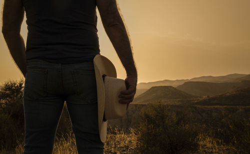 Silhouette of adult man holding cowboy hat standing on desert during sunset. almeria, spain