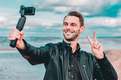 Young man blogging while standing at beach