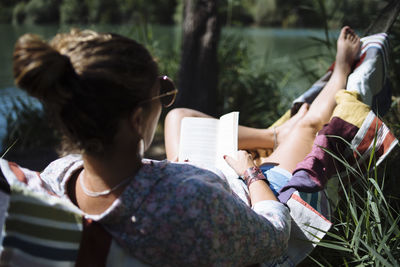 Woman with sunglasses reading a book lying on a hammock.