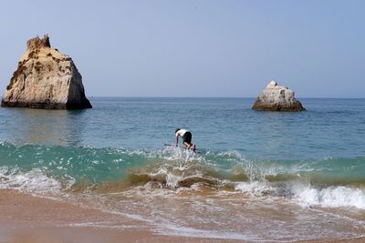 Man on rock in sea against clear sky