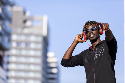 Man pointing while listening to music standing against sky