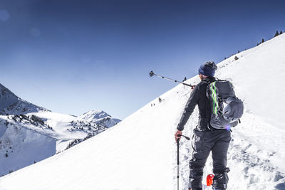 Rear view of man hiking on snowcapped mountain against sky