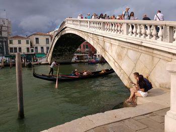 People sitting on bridge over river in city