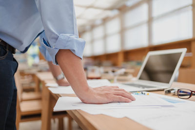 Midsection of man standing by papers on table