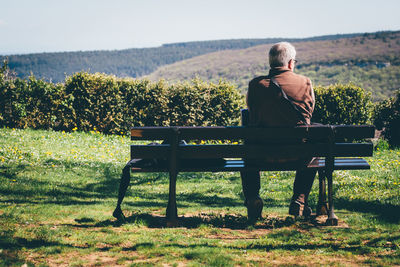 Rear view of senior man sitting on bench against mountain