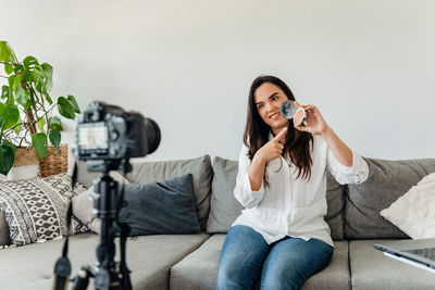 Beauty blogger using camera on tripod to record video about a make-up product