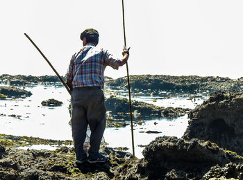 Man fishing on rock against sky