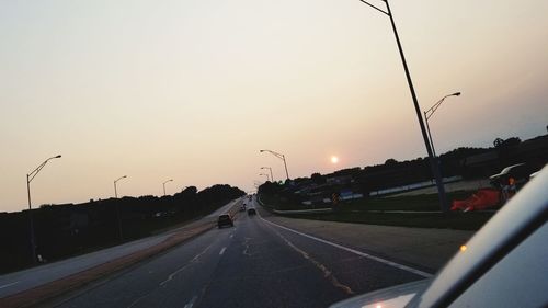 Vehicles on road against sky during sunset