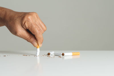 Close-up of hand holding cigarette against white background