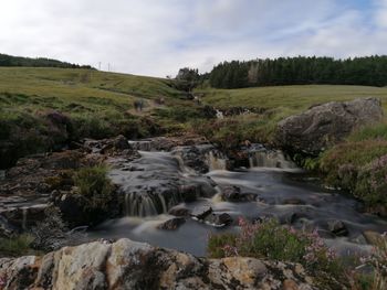 Scenic view of stream flowing through rocks against sky