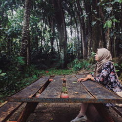 Side view of thoughtful woman sitting at rusty table against trees in forest