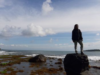 Portrait of smiling man standing on rock at beach against sky