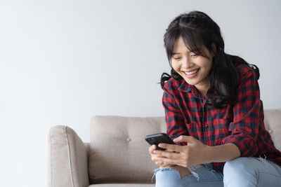 Smiling young man using mobile phone while sitting on sofa