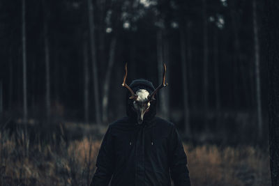 Person wearing taxidermy standing against trees in forest