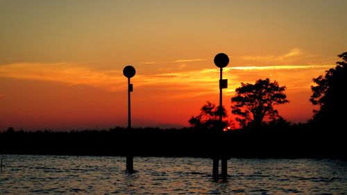 Silhouette trees by calm lake at sunset
