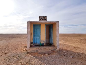 Abandoned outhouse on desert against cloudy sky