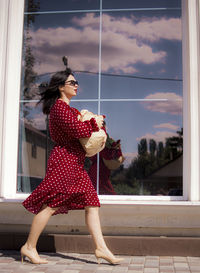 Side view of young woman with arms raised standing by window