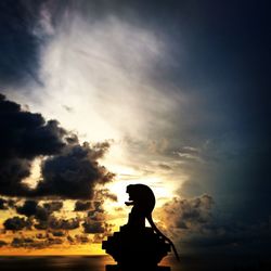 Silhouette monkey sitting against dramatic sky during sunset