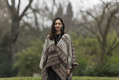 Portrait of young woman standing against trees