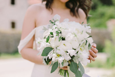 Midsection of bride holding white bouquet