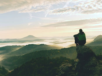 Mountain peak. man sit on sharp summit and enjoy spectacular view. bright morning sun shining in sky