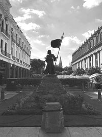 Statue of man holding a flag against buildings in city