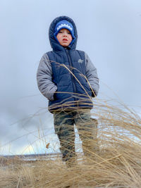 Low angle view of boy wearing warm clothing standing against sky