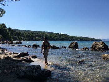 People standing on rocks by sea against clear blue sky