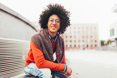 Portrait of afro young man sitting on bench in city