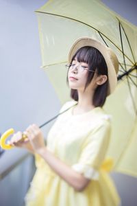 Close-up of young woman holding yellow umbrella while standing outdoors