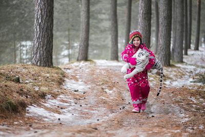 Girl in warm clothing carrying toy tiger while walking in forest during winter