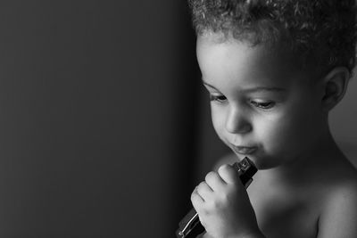 Cute boy holding musical instrument while standing against gray background