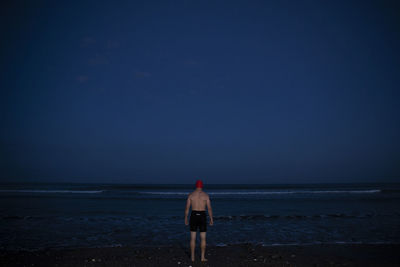 Rear view of woman walking at beach against clear sky