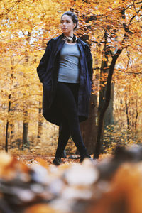 Full length of young woman standing in forest during autumn