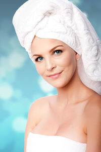 Portrait of young beautiful woman wrapped in a towel against blue background