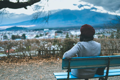 Rear view of woman looking at mountain while sitting on bench during winter