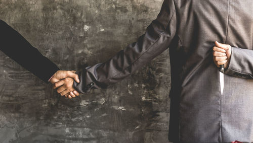 Close-up of businessmen shaking hands against wall