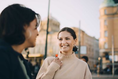 Smiling young woman looking at female friend in city