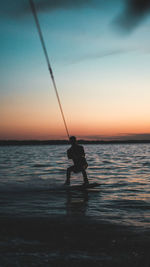 Silhouette of a man doing wakeboarding in a lake with mountains in the background